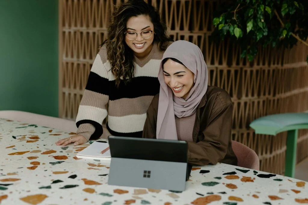 Overcoming Burnout: Rediscovering Joy in Your Work 3 | Mania Africa | maniainc.com Two women sitting at a table with a laptop. How Modern Management Selection Impacts the Likelihood of Employee Burnout - Mania Africa