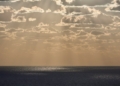 Sunlight streams through clouds over the ocean - A serene, misty horizon where the ocean meets a golden sky, symbolizing the transition between life and the unknown - The Paradox of Life at Death’s Edge: The Gift of Perspective and Lessons from Near-Death Experiences - Mania Lifestyle