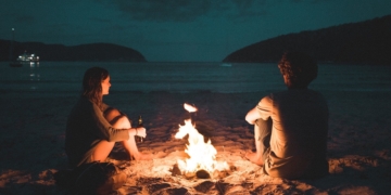 A man and woman sitting near a fire by the beach