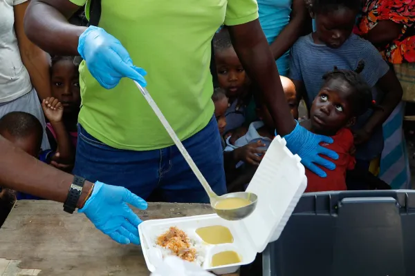Gangs and Insecurity: Investigating the Root Causes of Instability in Haiti 12 | Mania Africa | maniainc.com A social worker serving food to Haitian children | Gangs and Insecurity: Investigating the Root Causes of Instability in Haiti | Featured Stories on Mania Africa