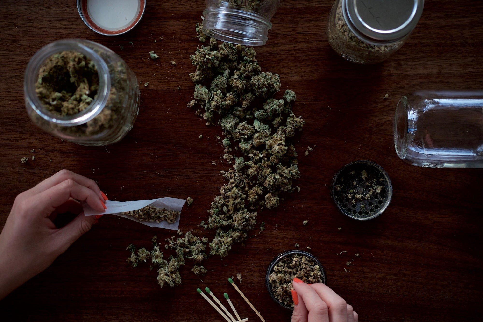 Health Benefits and Potential Risks of Cannabis: What You Need to Know 3 | Mania Africa | maniainc.com A person rolling cannabis buds into cigarettes with other buds in clear jars