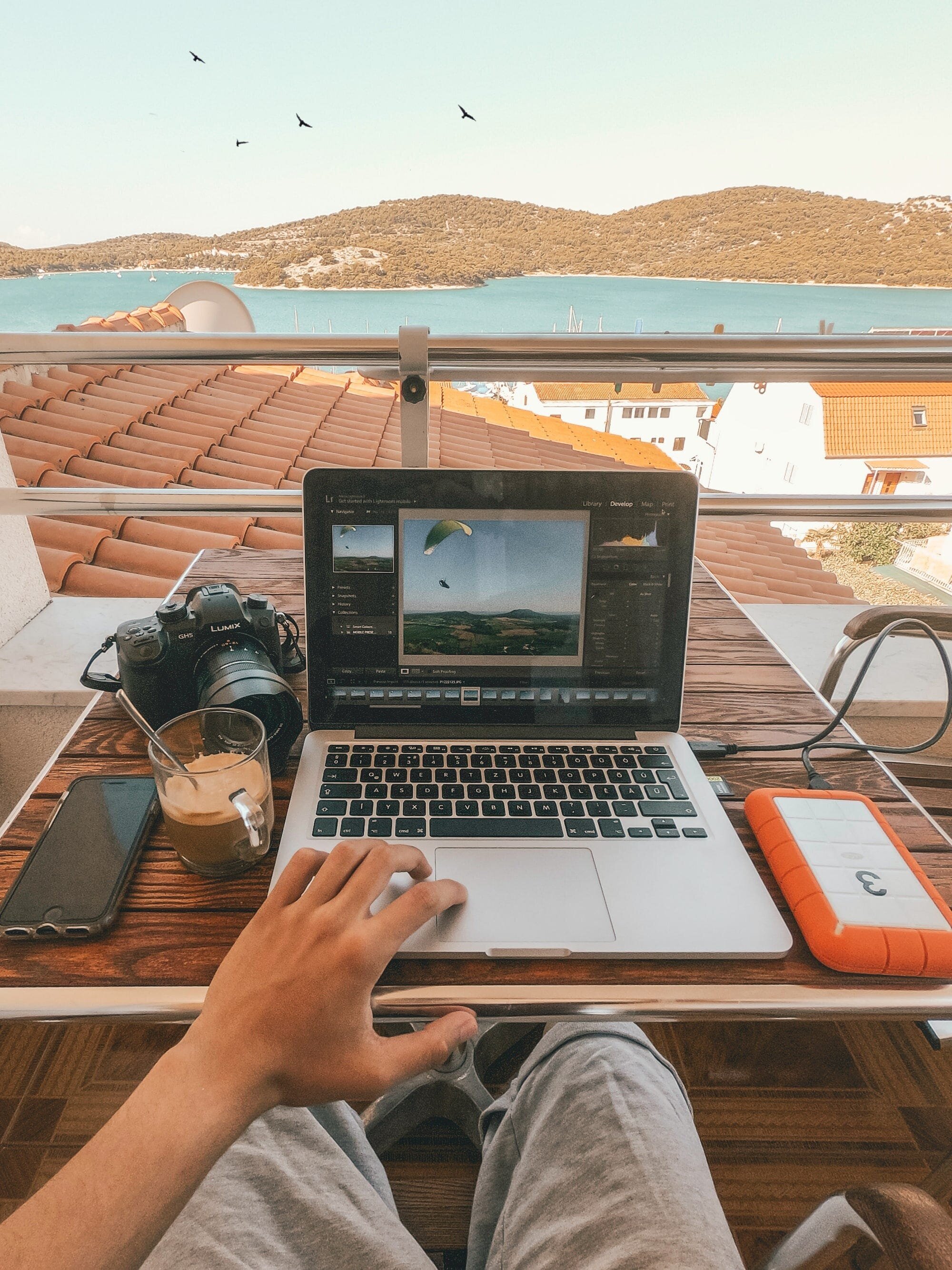 Remotasks Review: Everything You Need to Know About the Micro-Job Site for Remote Work Opportunities 11 | Mania Africa | maniainc.com An image of a person working on some video editing at a balcony just by a shoreline somewhere in Greece