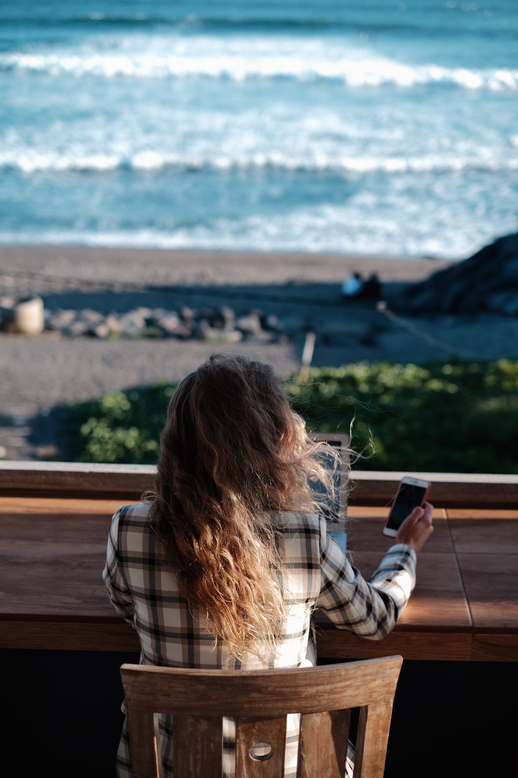 The Keys to Success on Fiverr: A Comprehensive Guide for Freelancers and Buyers 3 | Mania Africa | maniainc.com A woman sitting on an outside porch checking her phone while working on her computer